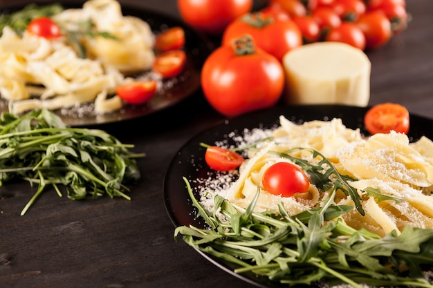 Piatto con tagliatelle, pomodorini e verde su tavola di legno