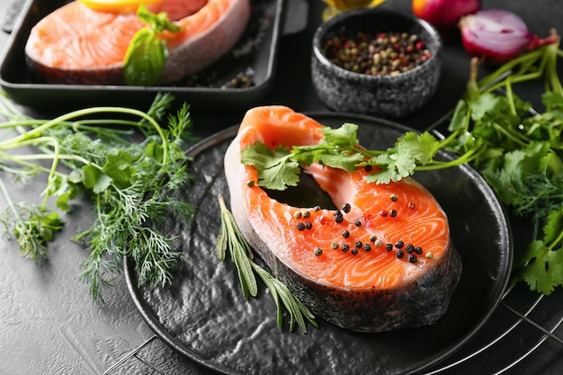 Piatto con tranci di salmone crudo, erbe e spezie su oscurità