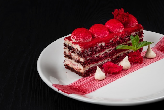 Piatto con un pezzo di deliziosa torta di velluto rosso su fondo di legno nero concetto di cibo e bevande