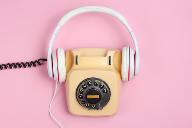 Piatto creativo in stile retrò. Telefono rotativo vintage con classici auricolari bianchi su sfondo rosa. Cultura pop.