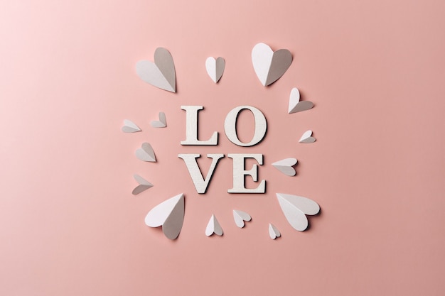 Piatto creativo laici di parola amore sulla parete di colore tenue con cuori di carta.
