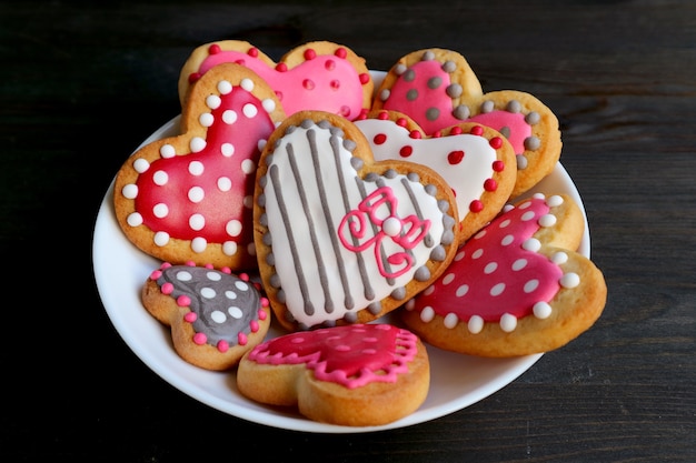Piatto del cuore fatto in casa a forma di con i biscotti a velo reale modellati punteggiati sulla tavola di legno colorata nera