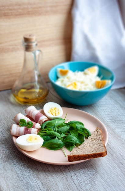 Piatto della colazione dell'alimento con le uova della pancetta del basilico verde delle foglie degli spinaci e un pezzo di pane di segale Insalata