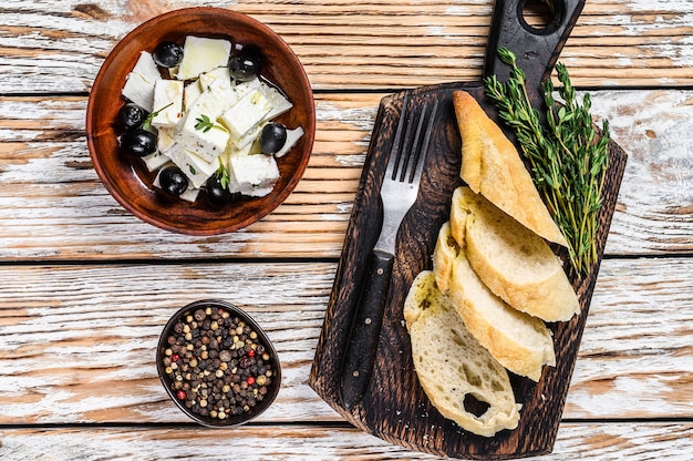 Piatto di antipasti con formaggio feta fresco, pane e olive. Tavolo in legno bianco. Vista dall'alto.