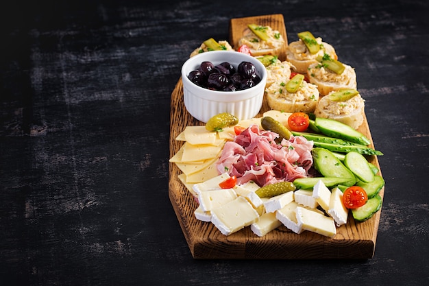 Piatto di antipasti con prosciutto, formaggio, tartine e olive nere su una tavola di legno. Vista dall'alto, dall'alto