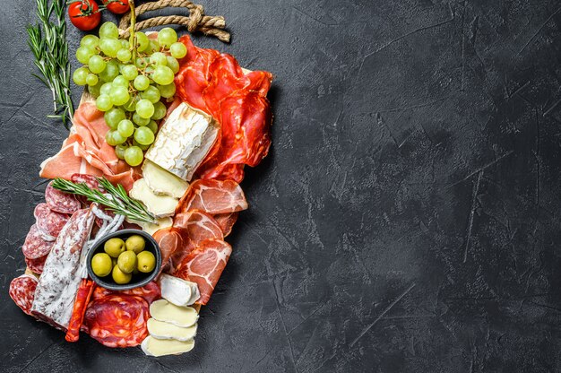 Piatto di antipasti di carne fredda con uva, prosciutto, fette di prosciutto, carne secca, salame di chorizo, fuet, camembert e formaggio di capra. Vista dall'alto.