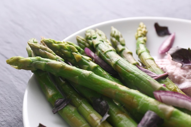 Piatto di asparagi freschi con cipolla rossa tritata su piatto bianco su fondo di legno grigio da vicino