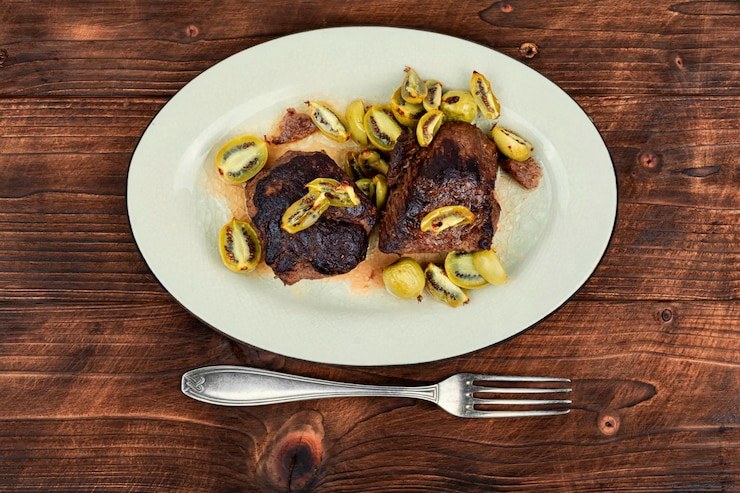 Foto piatto di bistecca di struzzo arrostita con salsa mini kiwi carne con bacche di kiwi su tavolo di legno