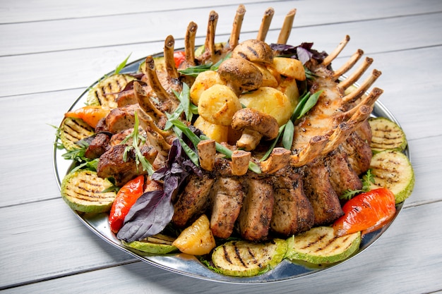 Piatto di carne con deliziosi pezzi di carne, insalata, costole, verdure grigliate e patate sul tavolo di legno bianco