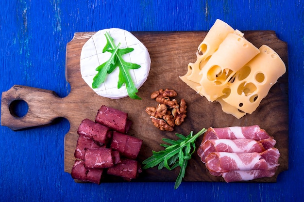 Piatto di carne e formaggio con noci su superficie di legno blu,