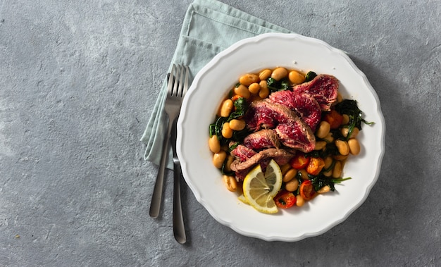 Piatto di cena con bistecca di manzo, fagioli bianchi, spinaci e pomodori vista dall'alto con spazio di copia