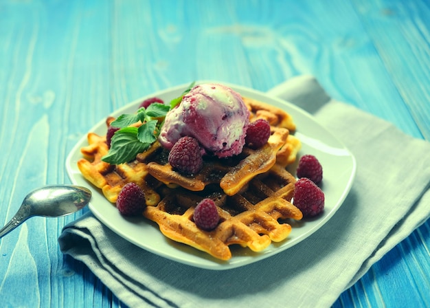 Piatto di cialde belghe con gelato e frutti di bosco freschi su sfondo di legno blu