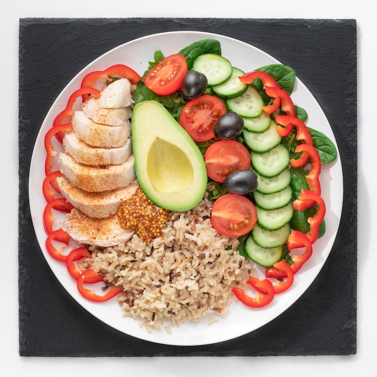 Foto piatto di cibo sano filetto di pollo, insalata, avocado e porridge di riso integrale. in un piatto bianco su un supporto di ardesia nera.