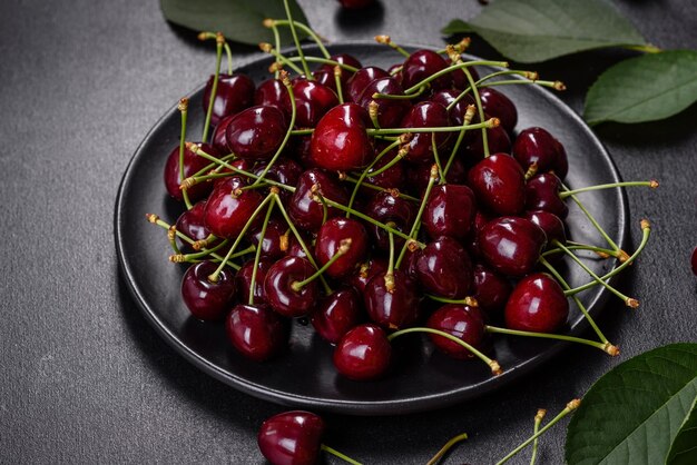 Piatto di ciliegie dolci fresche con foglie in gocce d'acqua su sfondo di pietra vista dall'alto