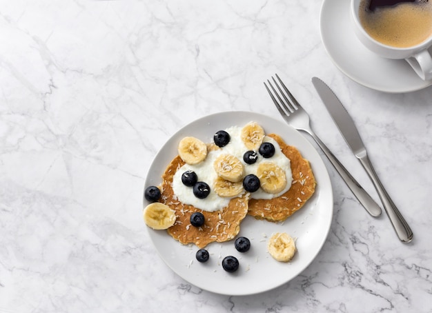 Piatto di colazione fatta in casa con frutti di bosco e tazza di caffè al tavolo di marmo.