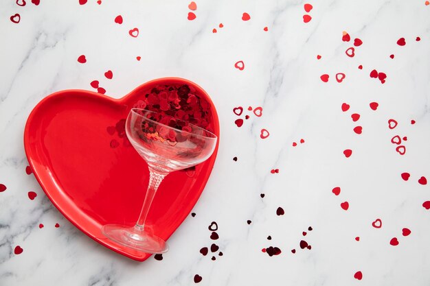 Piatto di cuore rosso del fondo della cena di San Valentino con vetro di champagne e coriandoli