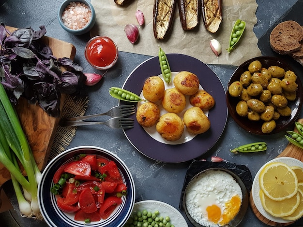 Piatto di delizioso tavolo da pranzo per due con patate fritte pomodori biologici insalata di olive cipolla verde melanzane uova su sfondo di pietra scura Cibo sano concetto vari cibi e spuntini