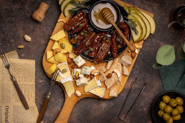 Piatto di formaggi con diversi formaggi, pomodori secchi, noci, miele e datteri su tavola di legno rustica.