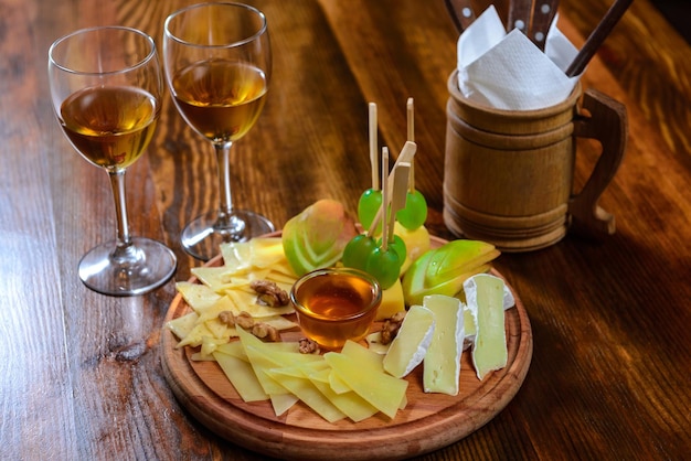 Piatto di formaggi con noci di miele e uva con bicchieri di vino bianco