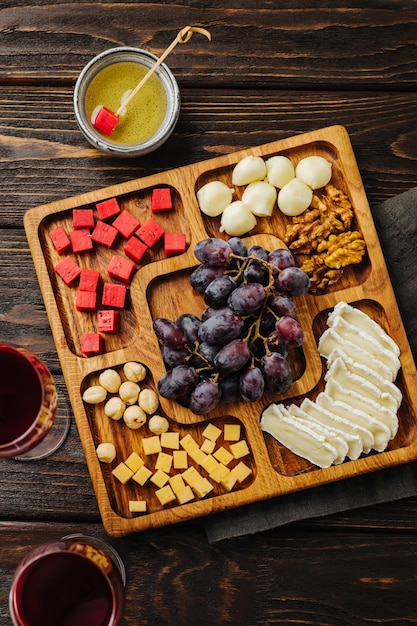 Piatto di formaggi e ciotola quadrata in legno per vino con snack