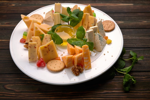 Piatto di formaggi, formaggi assortiti alla menta, frutta candita, miele e biscotti, su un piatto bianco, su uno sfondo scuro