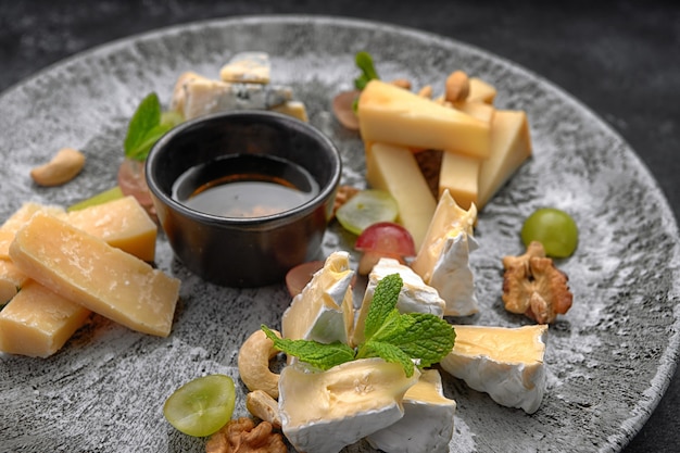 Piatto di formaggi, formaggi assortiti con menta, frutta candita, miele e biscotti, su un piatto