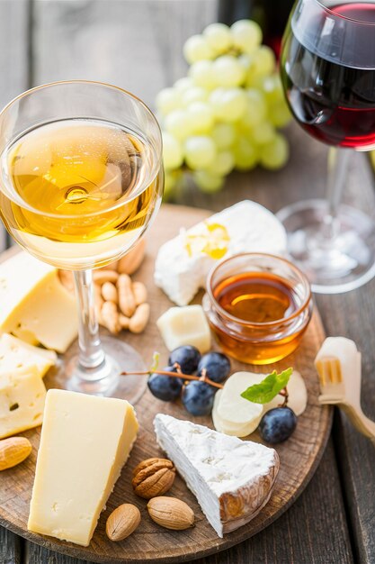 Piatto di formaggio con noci di miele e uva e vino bianco e rosso in bicchieri su un fondo di legno