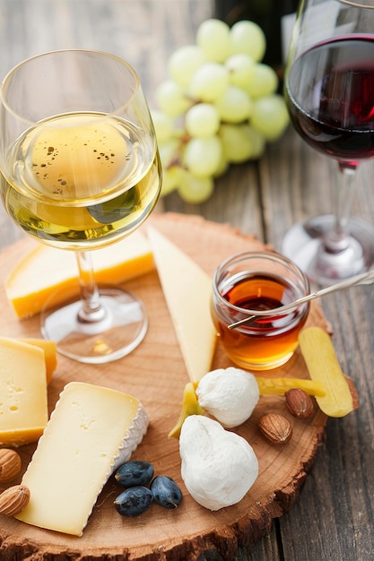 Piatto di formaggio con noci di miele e uva e vino bianco e rosso in bicchieri su un fondo di legno