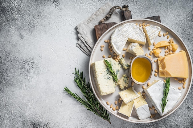 Piatto di formaggio francese con camembert, brie, gorgonzola, parmigiano, miele, noci ed erbe aromatiche. Sfondo bianco. Vista dall'alto. Copia spazio.