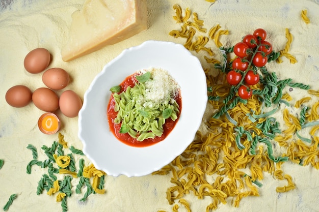 Piatto di fusilli in salsa di pomodoro in un piatto bianco sullo sfondo di farina, uova, pomodori