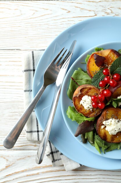 Piatto di insalata con pesca alla griglia su tavola di legno bianco