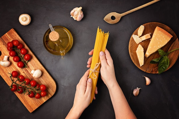 Piatto di laici donna mano che tiene gli spaghetti e gli ingredienti per cucinare la pasta italiana. Spaghetti, pomodori, olio, aglio, parmigiano. Vista dall'alto del concetto di cucina italiana tradizionale