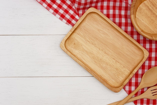 Piatto di legno rettangolo vuoto con forchetta cucchiaio e tovaglia rossa a quadretti su tavolo di legno bianco