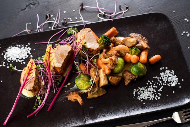 Piatto di medaglioni di carne e verdure su fondo di legno nero