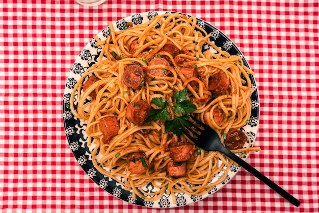 Piatto di pasta abbondante con salsa di pomodoro e salsiccia su un tavolo con una tovaglia a scacchi rossa