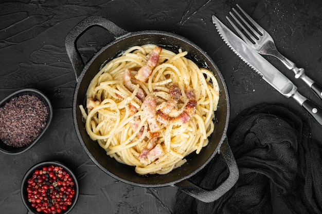 Piatto di pasta alla carbonara. Cucina tradizionale romana. Set di cibo italiano, in padella in ghisa, su sfondo di pietra nera, vista dall'alto piatta