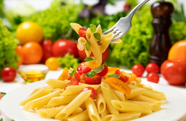 Piatto di pasta italiana cotta, penne rigate sulla forcella con pomodori e foglie di basilico