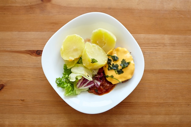 Piatto di patate bollite con insalata di verdure verdi e cotoletta su un tavolo di legno
