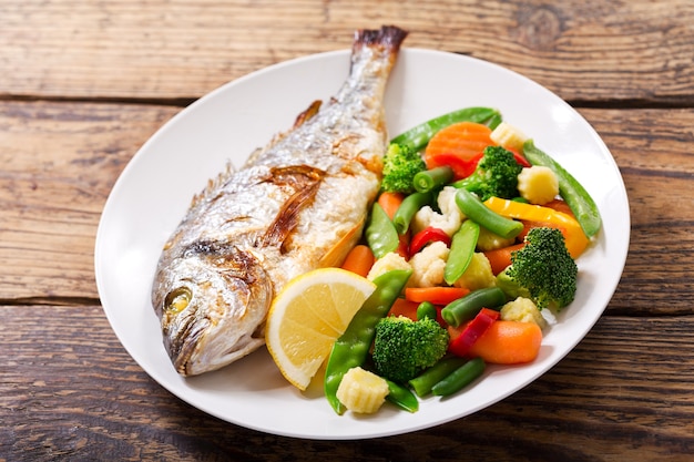 Piatto di pesce al forno con verdure sulla tavola di legno