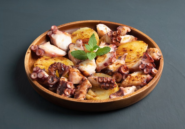 Piatto di polpo cotto servito con patate lesse a fette, paprika affumicata e olio d'oliva. sul tavolo rustico