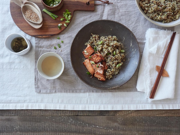 piatto di quinoa e salmone sul tavolo su tovaglia di lino bacchette e utensili in legno tè servito in ceramica