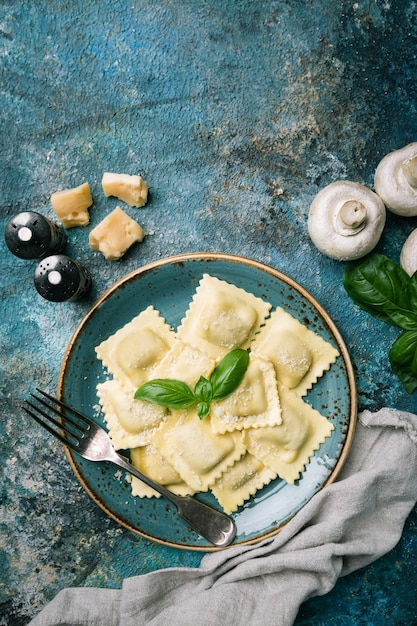 Piatto di ravioli con funghi e formaggio decorato da basilico su pietra scura