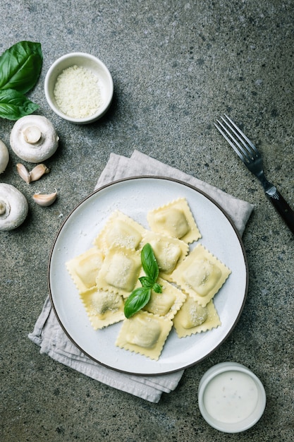 Piatto di ravioli con funghi e formaggio decorato da basilico su pietra scura