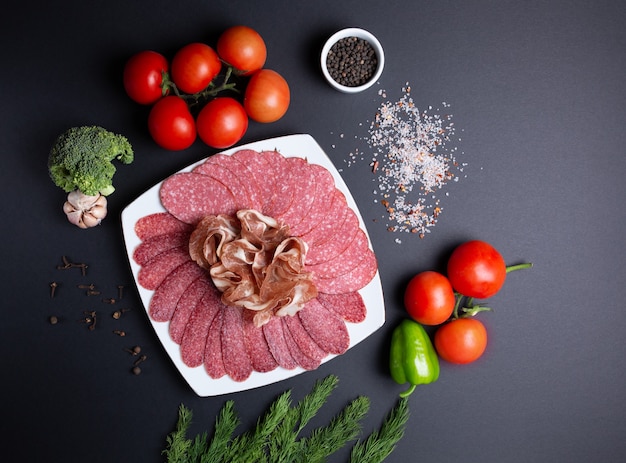 Piatto di salsiccia e carne, su fondo nero con pomodori, aneto, aglio e broccoli