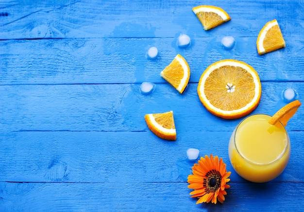 Piatto di succo d'arancia fresco guarnito con una fetta di arancia matura e fiori sul tavolo di legno blu