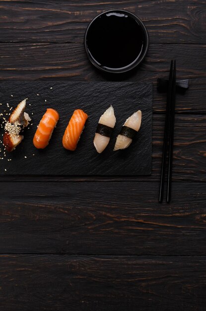 Piatto di sushi colorato nel ristorante giapponese, con bacchette e salsa di soia su sfondo di legno scuro, verticale, vista dall'alto, piatto