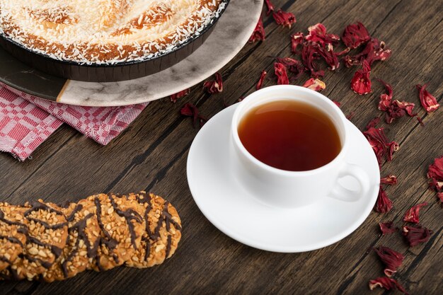 Piatto di torta dolce con granelli di cocco, biscotti e tazza di tè su una superficie di legno