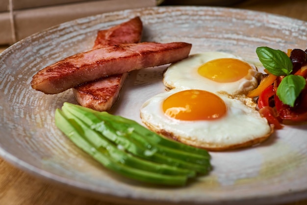 Piatto di uova fritte con pancetta e avocad sul tavolo di legno Colazione inglese sul tavolo