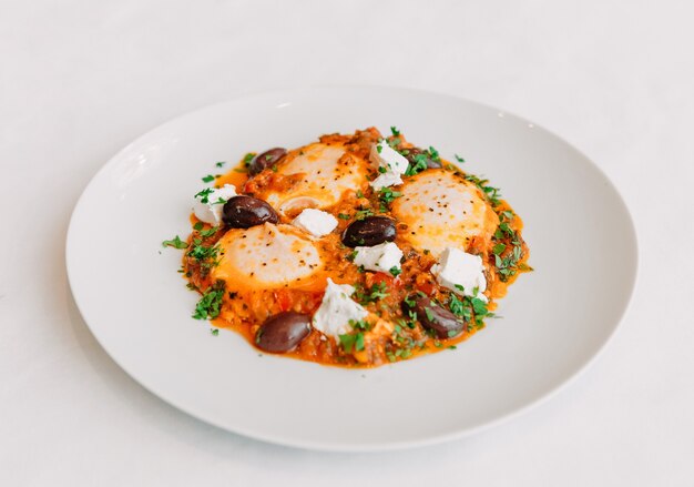 Piatto di uova strapazzate da tre uova con olive e formaggio feta in una vista dall'alto piatto bianco