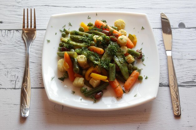 Piatto di verdure saltate in padella su un tavolo di legno con vista sull'insalata estiva in un piatto bianco